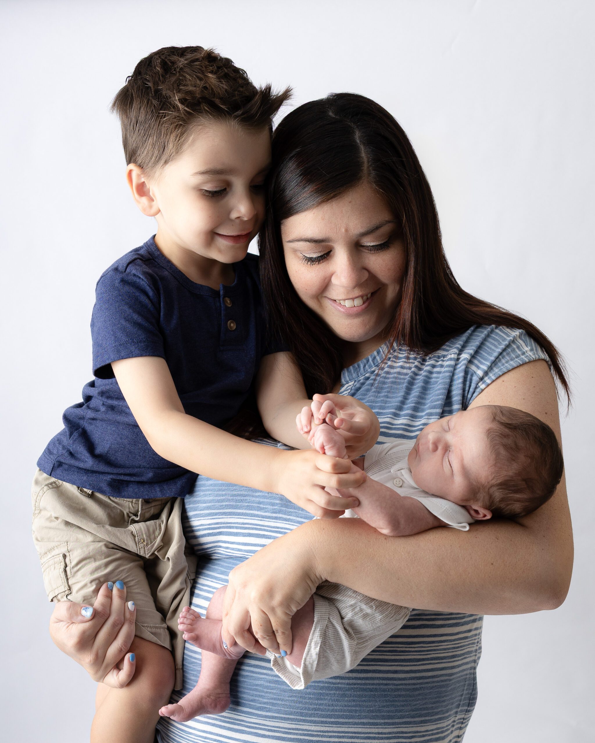 Mom holding her son and his newborn brother as they both admire the new baby.