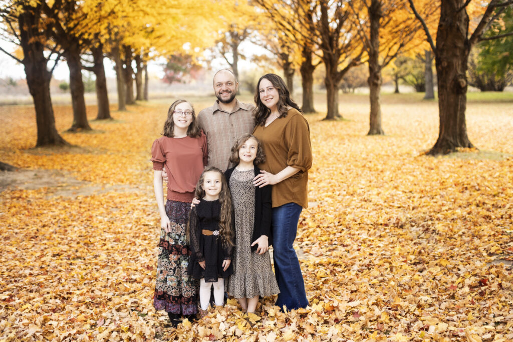 Family of five posing for fall family portraits among a row of trees at For-Mar Nature Preserve.