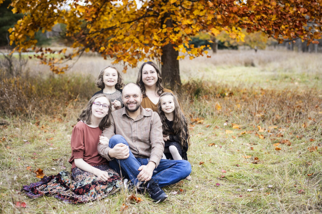Fall portrait of a family of five sitting under a tree at For-Mar Nature Preserve in Burton, Michigan.