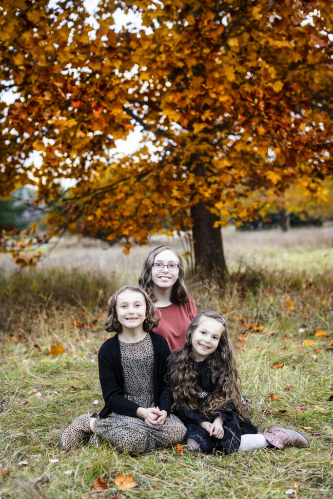 Three sisters in a seated pose for fall portraits in Genesee County, Michigan.