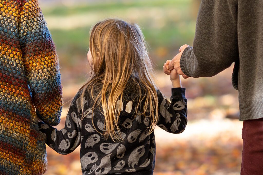 Little boy holding mom and dad's hands as they walk through the woods during a fall family session.